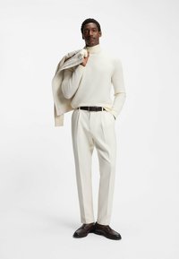 Crème coltrui, op maat gemaakte witte broek en donkerbruine schoenen. Lichte jas over de schouder gedrapeerd. Gladde textuur, minimalistisch design.