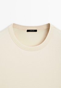 Beige T-shirt met korte mouwen en een ronde hals, gemaakt van zachte stof. Het label toont "Massimo Dutti" en "Made in Portugal."