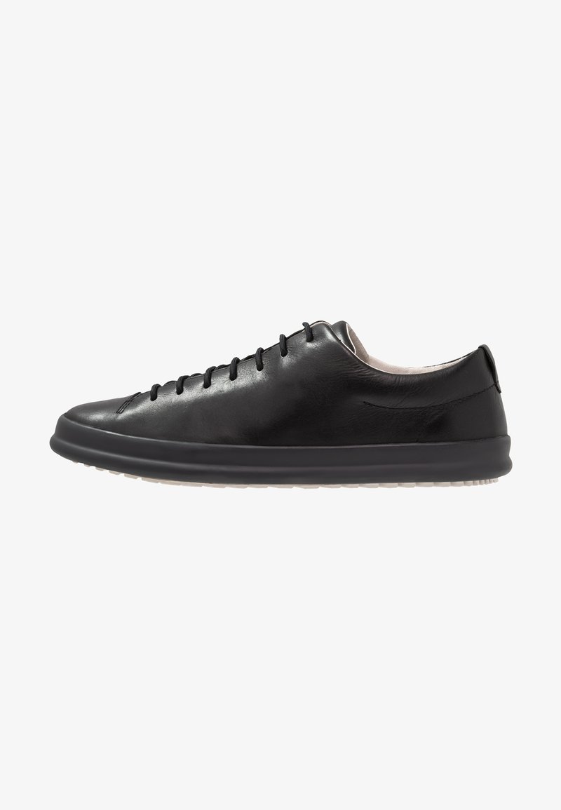 Black leather sneaker features a rounded toe, minimal lacing, a smooth texture, and a contrasting white rubber sole. Subtle brand detailing visible.