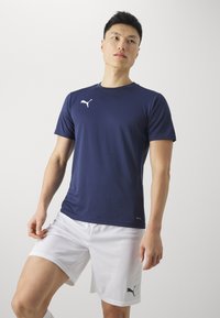 Mørkeblå idrettsgenser med korte ermer og Puma-logo i hvitt, kombinert med hvite shorts med en liten svart logo.