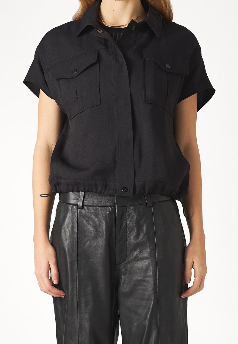 Chemise noire à manches courtes avec deux poches frontales, un col boutonné et un ourlet élastique froncé. Fabriquée en tissu léger, offrant une coupe décontractée.