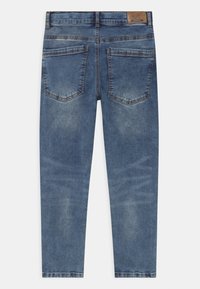 Vista trasera de unos vaqueros de denim azul con áreas descoloridas, dos bolsillos traseros, pasadores para el cinturón y una etiqueta de cuero marrón en la cintura.