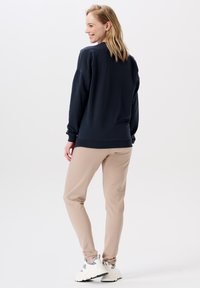 Marineblauwe sweatshirt met een relaxte pasvorm en ribgebreide manchetten, gecombineerd met beige tapered sweatpants en witte sneakers met grijze accenten.