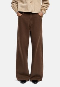 Brązowe spodnie typu wide-leg z bawełny, o gładkiej fakturze, z przednimi kieszeniami i swobodnym krojem, w połączeniu z czarnymi butami.