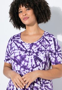 Lila Batik-Kleid mit kurzen Ärmeln, rundem Ausschnitt und geraffter Taille. Weicher Stoff mit einem wirbelnden Muster in verschiedenen Lilatönen.