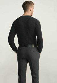 Czarny sweter z dzianiny o teksturowanym wzorze, zestawiony z szarymi dopasowanymi spodniami z dwiema tylnymi kieszeniami oraz czarnym skórzanym paskiem.