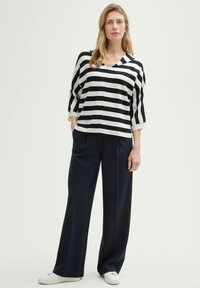 Top en tricot à rayures noir et blanc avec un col en V, associé à un pantalon large bleu marine et des baskets blanches. Tissu texturé, coupe décontractée.