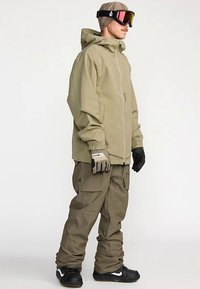 Snowboard jacket in light olive green, featuring a zip closure and adjustable hood, paired with matching cargo pants and gloves.