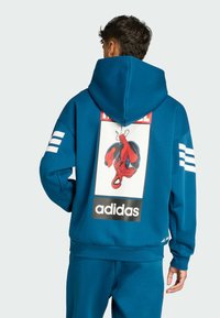 Blå huvtröja med en stor Spider-Man-grafik på baksidan och tre vita ränder på varje ärm. Mjuk tyg, avslappnad passform.