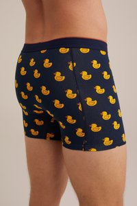 Herrers boxershorts i marinblått tyg med mönster av gula badande ankor; elastisk midja med röda accenter, slät textur.