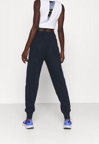 Navy blue joggers with cuffed ankles, made of cotton blend fabric. Paired with a fitted white cropped top featuring a back cutout design.