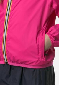Giacca leggera rosa con polsini elasticizzati, chiusura con zip caratterizzata da righe gialle e grigie, e tasche laterali.