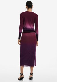 Abito lungo viola con sfumatura, maniche lunghe, tessuto morbido, bustino aderente e gonna svasata. Tacchi a strappo neri completano l'outfit.