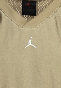 Jasno beżowa, sportowa koszulka z dekoltem w serek, wykonana z gładkiego materiału; posiada białą, haftowaną na piersi logo Jumpman.