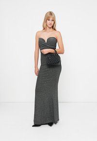 Trägerloses, silbernes Glitzer-Abendkleid mit herzförmigem Ausschnitt, taillierter Silhouette und langer Länge. Kombiniert mit einer kleinen schwarzen Handtasche.