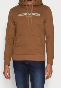 Brown hoodie with a kangaroo pocket, drawstring hood, and white "JACK & JONES" logo. Fabric appears soft with a smooth texture.