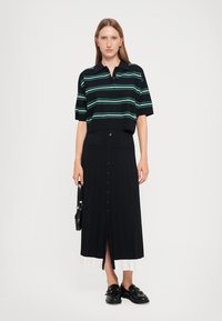 Marineblauw gebreide polo met horizontale strepen in teal en wit, gecombineerd met een lange marineblauwe geribbelde rok met knopen aan de voorkant en een zijsplit.