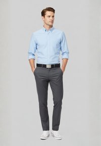 Light blue button-up shirt, gray trousers, black belt with silver buckle, and white sneakers. Simple, tailored design with long sleeves.