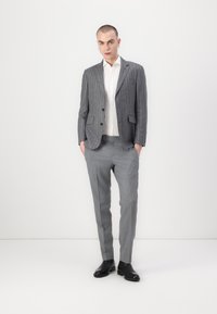 Completo grigio a righe sottili con giacca su misura e pantaloni abbinati, abbinato a una camicia bianca e scarpe in pelle nere. Tessuto di consistenza liscia.