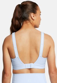 Lichtblauwe sportbeha van glad materiaal, met brede schouderbanden voorzien van het 'Under Armour' logo en een haaksluiting aan de achterkant.