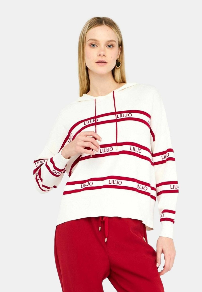 Felpa bianca con cappuccio, strisce orizzontali rosse e testo del logo, caratterizzata da una vestibilità rilassata e maniche lunghe, abbinata a pantaloni jogger rossi.