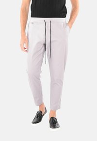 Pantaloni grigi chiari tapered con vita elastica e lacci, abbinati a scarpe nere slip-on. Tessuto liscio, design minimalista.