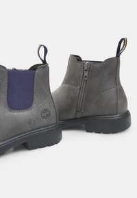Botines de ante gris con paneles elásticos en azul marino, cremalleras laterales y tiradores. Suelas de goma negra con un diseño texturizado para mayor agarre.