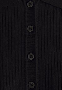 Černý žebrovaný svetr se zapínáním na knoflíky vpředu, obsahuje šest černých kulatých knoflíků a strukturovaný límec. Celkově měkká textura látky.