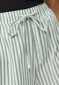 Shorts de pyjama rayés en tissu blanc avec des lignes verticales vertes, dotés d'une taille élastique et d'un cordon de serrage pour l'ajustement.