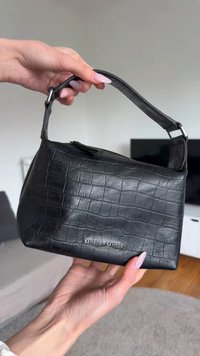 Borsa a mano in pelle nera con effetto coccodrillo e manico corto, tenuta da due mani con unghie rosa chiaro, che mostra il nome del marchio "Samsøe Samsøe."