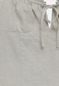 Section de jupe en lin beige avec taille élastique froncée et détail de passants de ceinture en tissu nouée.