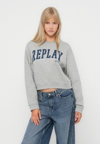Šedá skrátená mikina s potlačou "REPLAY" v námorníckej modrej, s okrúhlym výstrihom a mäkkou textúrou, kombinovaná so širokými džínsovými nohavicami modrej farby.