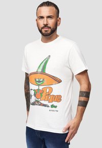 Hvid bomuldst-shirt med et farverigt tegneserie-graphic af en karakter i en sombrero, med teksten "Pique" i orange nedenfor.