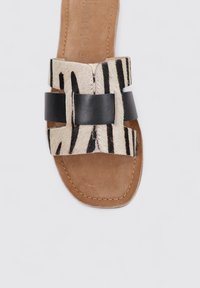 Sandalia de punta abierta con una plantilla de cuero marrón. La parte superior presenta un material de pelo de cebra con patrón, acentuado con una correa de cuero negra.