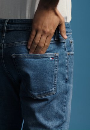 Χέρι που βάζει στο πίσω τσέπη μπλε τζιν με μικρό κόκκινο, λευκό και μπλε λογότυπο της μάρκας στην τσέπη.
