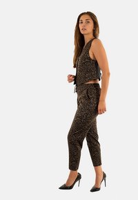 Haut court à imprimé léopard et pantalon fuselé assorti en tissu marron et noir. Le mannequin porte des talons hauts noirs, avec un motif texturé sur l'ensemble.