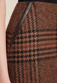 Falda de espiga en marrón y negro con tejido texturizado, que presenta un acento en forma de bolsillo de cuero oscuro en el lado.