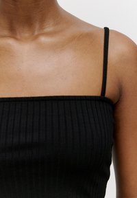 Schwarzes geripptes Tanktop mit schmalen Trägern, das einen quadratischen Ausschnitt und eine glatte Textur aufweist, Nahaufnahme des Oberkörperbereichs und der Schulterpartie.