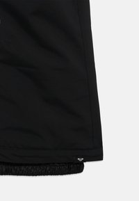 Sort yderbeklædningsstof med et lille syet mærke, der har et hvidt hjerteformet logo tæt på den elastiske kant.
