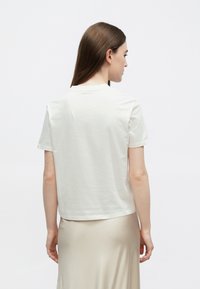 Balta kokvilnas T-krekls ar īsām piedurknēm, apaļu kakla izgriezumu un brīvu piegriezumu. Gluda tekstūra, minimālistisks dizains. Valdzināts kopā ar neitrālu svārku.