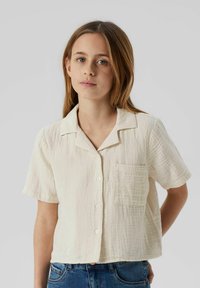Camisa de algodón de manga corta y cuello en color blanco roto, con un bolsillo en el pecho y un diseño de tela texturizada con costuras visibles.