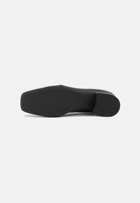 Semelle de chaussure noire plate avec une surface en caoutchouc texturée et un léger talon. Présente une forme arrondie et une finition lisse, avec un branding subtil.