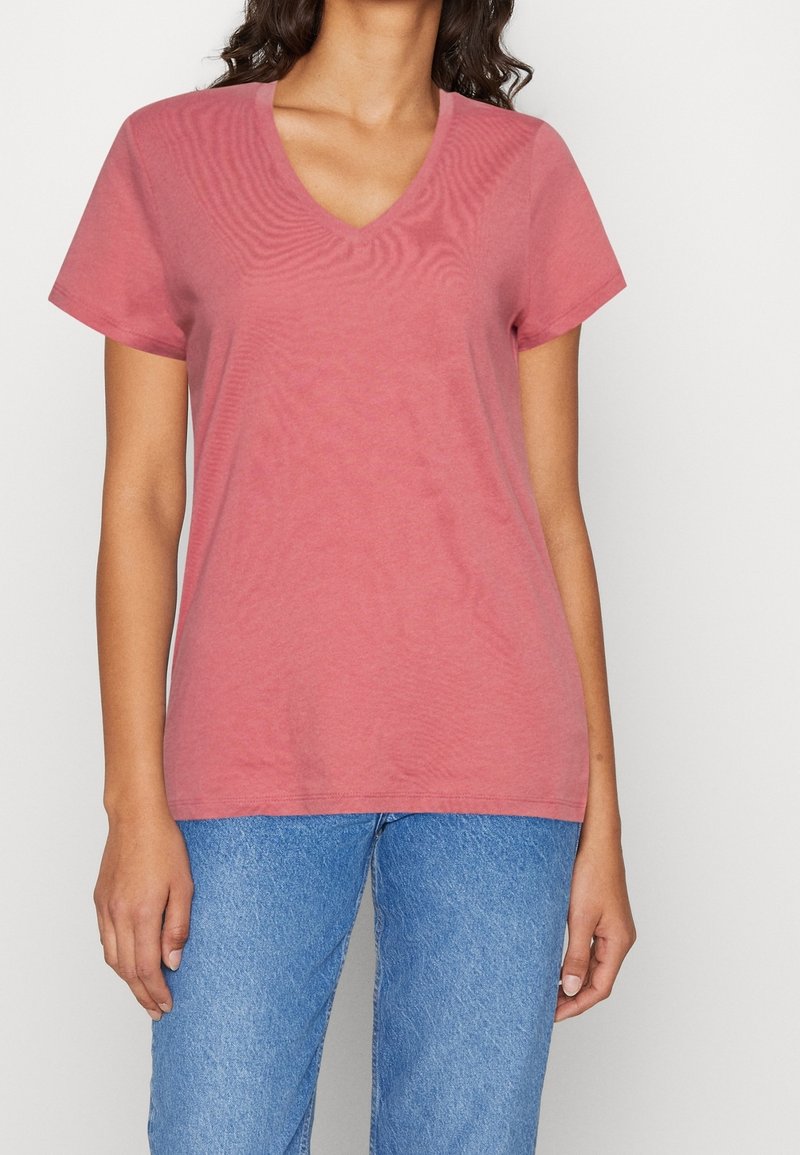 Lyserød bomulds t-shirt med V-hals og korte ærmer, parret med blå denim jeans. Stoffet har en glat tekstur.