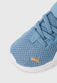Baskets en mesh bleu avec une surface texturée, arborant un logo orange et une sangle velcro. Semelle blanche avec un bout arrondi et un design minimaliste.