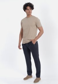 Beige T-shirt met korte mouwen, donkerblauwe broek, casual beige schoenen. Glad materiaal, comfortabele pasvorm en geen zichtbare patronen of logo's.