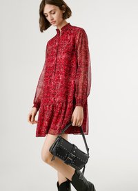 Vestido floral rojo con mangas largas transparentes y cuello alto, con un dobladillo de volantes en capas. Bolso negro con tachuelas y asa corta. Botas negras hasta el tobillo.