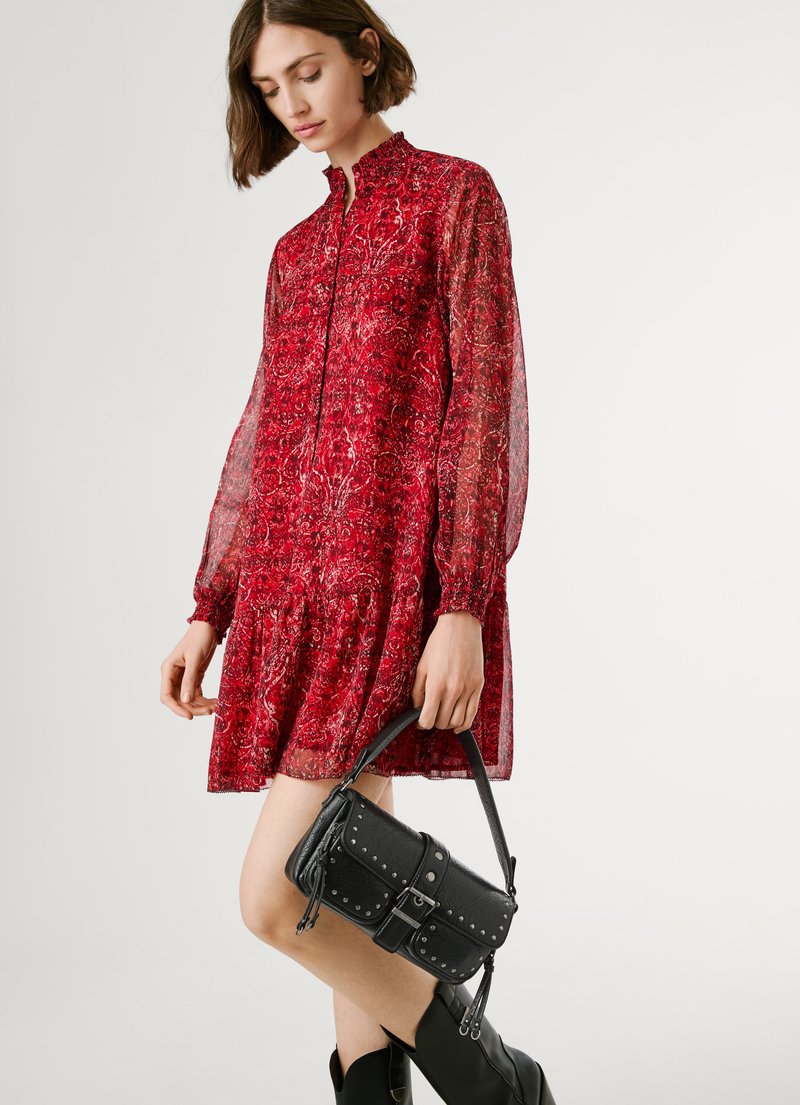 Vestido floral rojo con mangas largas transparentes y cuello alto, con un dobladillo de volantes en capas. Bolso negro con tachuelas y asa corta. Botas negras hasta el tobillo.
