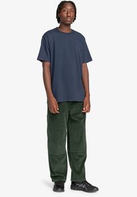 Marineblå bomulds T-shirt med rund hals, parret med grønne kordfløjspants med forlommer og en afslappet pasform. Sorte sneakers fuldender looket.