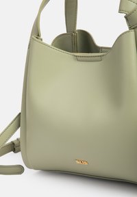 Μικρή ανοιχτοπράσινη δερμάτινη τσάντα με κοντές λαβές, αποσπώμενο ιμάντα ώμου και μικρό χρυσό λογότυπο κοντά στη βάση.