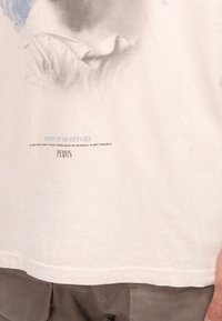 Cremefarbendes Baumwoll-T-Shirt mit einem verblassten Grafikdruck, der den Text "Point of No Return" sowie weitere Details darunter zeigt, mit einem geraden Saum geschnitten.